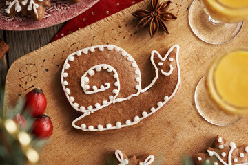 Snail shaped gingerbread Christmas cookie with two glasses of Eiecognac on a wooden table