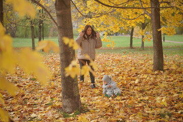 Little boy playing in autumn park. Child on yellow fallen leaves on a sunny autumn day.