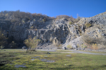 Quarry with rocky cliffs surrounded by sparse vegetation and a grassy foreground. © Planitia Spectra