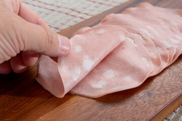 A view of a hand folding a slice of mortadella.