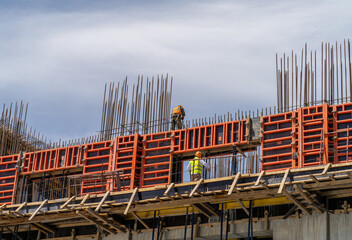 Two construction workers are assembling concrete formwork. Construction site, assembly of modern equipment and steel reinforcement for concrete structures during the construction of building walls. © Sergei
