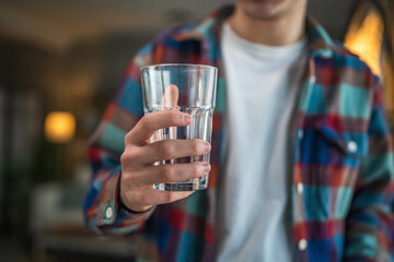 close up of yong man stand with glass of water and smile at home