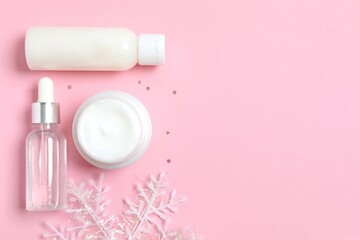 Winter skin care concept. Cosmetic products packaging design. Dropper bottle with serum, moisturizer cream jar and snowflake on color background. Flat lay, top view.
