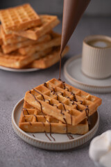 photo Delicious homemade waffles with rich chocolate drizzle served with a hot cup of coffee, perfect for breakfast or brunch indulgence at home or on a relaxing weekend
