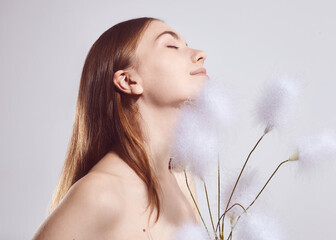 A beautiful brunette woman with fluffy plants in her hands poses on a light background....