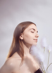 A beautiful brunette woman with fluffy plants in her hands poses on a light background....