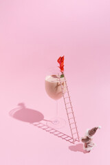 A whimsical scene unfolds as a miniature Santa figure scales a ladder leading to a glass filled with a refreshing drink. The soft pink backdrop enhances the playful atmosphere. Copy space.