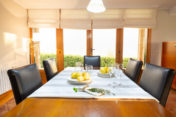 Natural wood dining table with five black leather chairs, dining room with French doors and white...