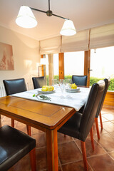 Natural wood dining table with five black leather chairs, dining room with French doors and white blinds, white tablecloth with gray stripes, champagne glasses, plates and lemons, chalet, country hous