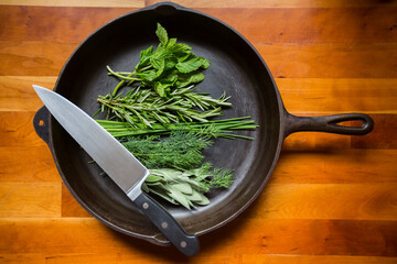 Fresh organic green herbs in an iron skillet with a sharp knife, sage, rosemary, chives, dill, parsley. Healthy vegan vegetarian eating diet.