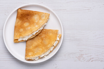 Delicious golden crepes filled with creamy cheese served on a white plate
