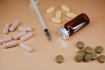 A syringe with a thin sharp needle, an injection ampoule and multi-colored pills