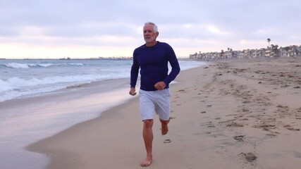 A mature 66 year old man jogging at the beach in Southern California. Slow Motion. - Powered by Adobe