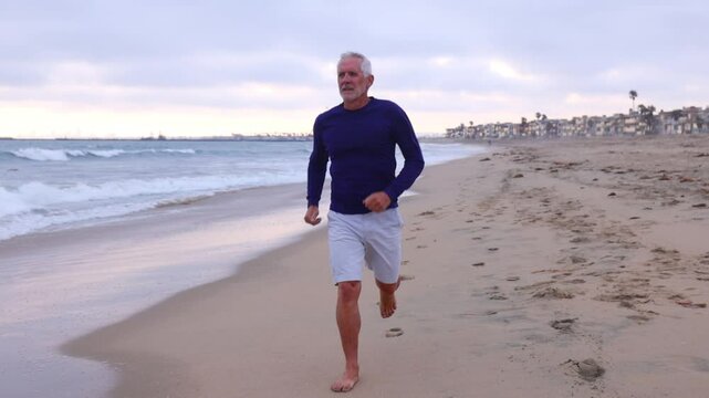 A mature 66 year old man jogging at the beach in Southern California. Slow Motion.