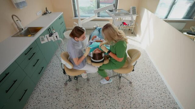 Blonde Woman Dentist with Assistant Treat Teeth of Female Patient with Special Instrument. Treatment of Caries and Plaque in Dental Clinic. Concept of Medicine and Healthcare. Slow Motion.