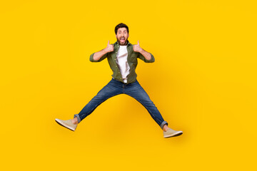 Full size photo of nice young man jump show thumb up wear shirt isolated on yellow color background