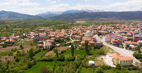Obraz premium Aerial view of typical Turkish small town Yesildag of Burdur province on sunny spring day with snowy mountain range in background..