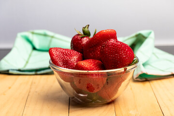 bol de cristal con frutos rojos, frutillas y fresas sobre madera al fondo un paño de cocina de tela verde esmeralda con líneas verde oscuro
