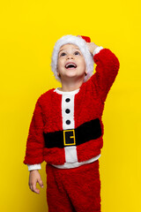Joyful child wearing Santa costume with fluffy texture against bright yellow background during holiday season