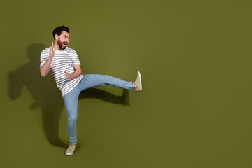 Photo of cheerful crazy funny man wear striped stylish clothes kick leg empty space isolated on khaki color background © deagreez