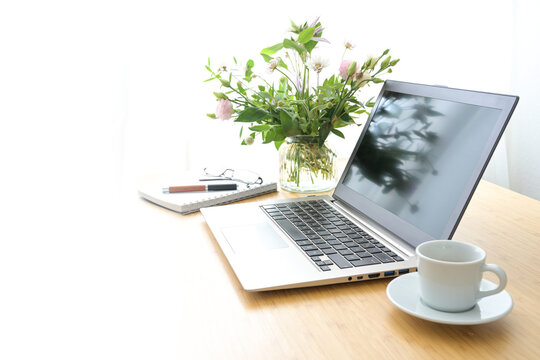 Bright feminine workspace with laptop, coffee and flowers on a wooden table in a cozy home office, background fades to white, concept for business, study or creative work, copy space