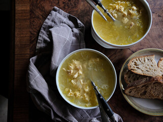 Bowls of chicken broth with white meat, served with slices of sourdough bread