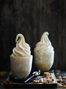 two ice cream sundaes filled with caramel soft ice cream, on a dark wooden background