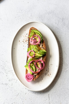 An appetizing open-faced sandwich featuring sliced avocado and pickled red onions on a rustic slice of bread, garnished with spices.