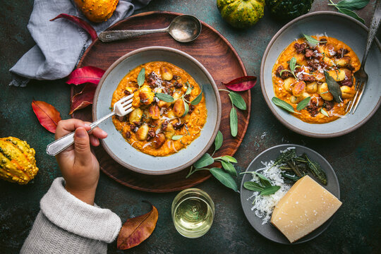A close shot of a bowl of crispy gnocchi in pumpkin sauce with sage and sausage arranged on a dark green surface