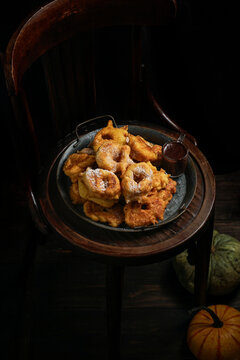 pumpkin donuts, spanish sweet dish, Bu&ntilde;uelos de calabaza, la receta tradicional valenciana, wooden chair. The dark background, autumnal theme, big pumpkin under chair