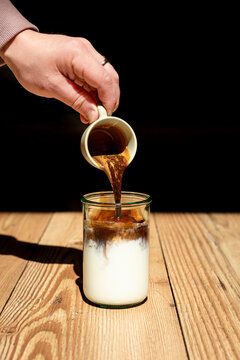 Hand pouring iced coffee into glass.