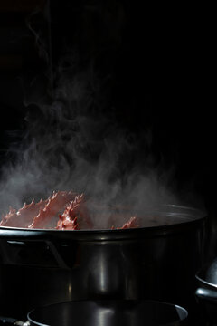 Whole king crab boiling in a metal pan, hot steam on a black background