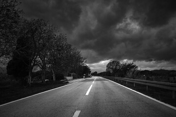 Monochrome Rainy Road with Speed and Danger Leading to Mountains Under Dramatic Skies