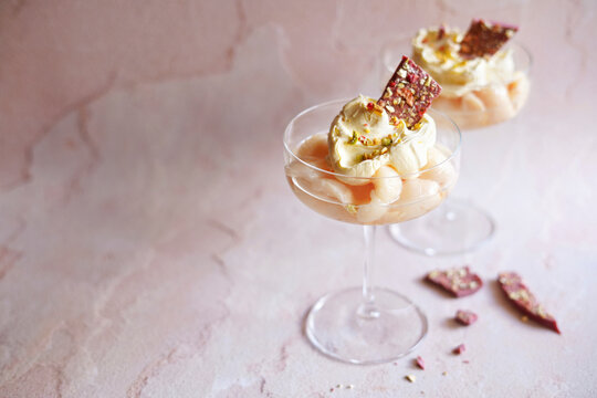 Lychees served with dollops of double cream and shards of ruby chocolate pistachio bark. Horizontal orientation with negative space.