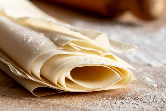 On a wooden cutting board, rolled layers of phyllo dough are arranged diagonally