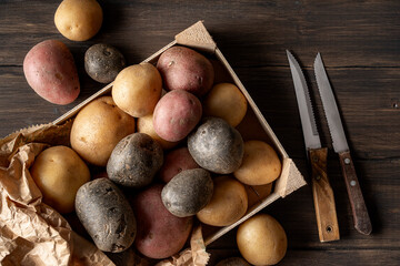Group of different type of potatoes: purple potatoes, red potatoes, and russet potatoes, on dark wooden table.