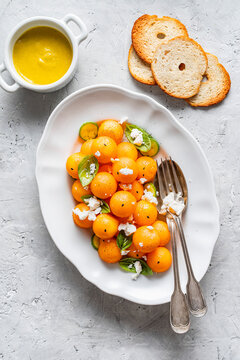 Melon balls with rocket, feta, and cucumber slices, garnished with basil leaves and pepper. Small bowl of sauce made with melon and cucumber, salt, oil. Top view. Copy space.