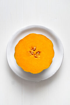 Melon cut in half placed on a white plate, on a white wooden background. Top view..