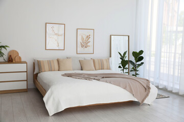 Large bed, houseplant and full-length mirror near window in room. Stylish bedroom interior