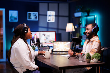 Cheerful african american content creators producing podcasts and hosting live chats for online listeners. Black man and woman broadcasting their talk show via recording audio equipment.