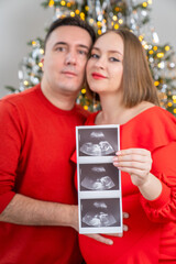 winter holiday pregnancy. Husband and wife future parents are holding baby ultrasound pictures. Happy couple red outfit. Merry Christmas and happy new year