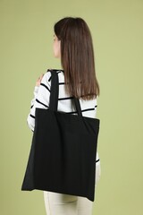 Woman with blank black shopper bag on color background, back view. Mockup for design