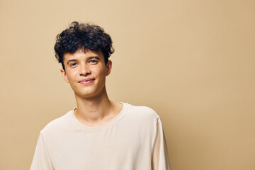 Young man smiling against a light beige background, casually dressed in a plain shirt, conveying a...