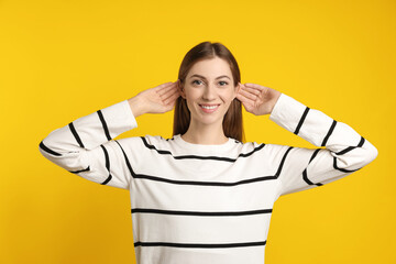 Woman showing hand to ear gesture on dark yellow background