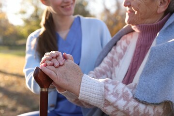 Elderly woman with walking cane and her caregiver in park, closeup