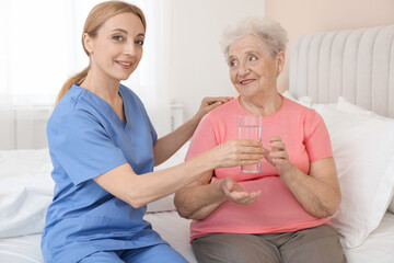 Healthcare worker giving glass of water to senior patient at home