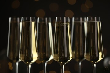 Champagne in glasses on dark background with blurred Christmas lights, closeup. Bokeh effect