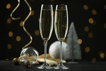 Delicious champagne in glasses and Christmas decor on black table against blurred lights