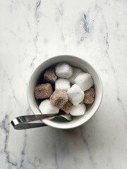  a small white bowl containing an assortment of sugar cubes. The cubes are both white and brown, suggesting a mix of refined white sugar and unrefined or raw brown sugar.