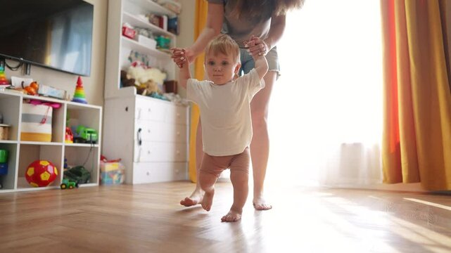 The first steps baby of learning to walk in home. Child toddler family concept. A baby is taking the first steps on its legs. lifestyle A baby takes the first steps on his legs at home.